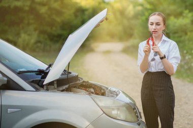 Arabası bozulduktan sonra yol kenarındaki genç kadın hasarı görmek için kaputu açtı.