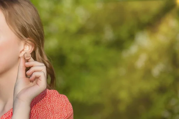 Close-up Of Female Hands Putting Hearing Aid In Ear. Modern digital in the ear hearing aid for deafness and the hard of hearing patients