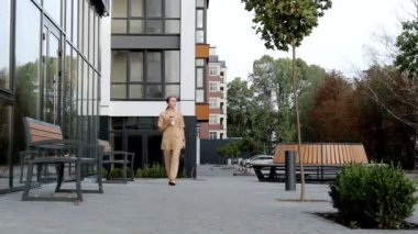 Kendine güveni tam bir iş kadını, modern iş alanının yakınındaki otoparkta yürüyor. Genç sarışın kadın Smartphone 'da mesaj atıyor ve yürürken kahve içiyor. Başarı