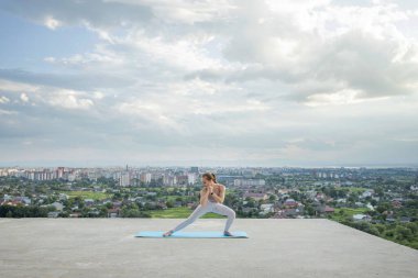Güneşli bir sabahta uzun at kuyruklu kaslı genç bir kadının yan görüntüsü. Güzel kız egzersiz yapıyor, şehir arka planında vücudunu ısıtıyor..