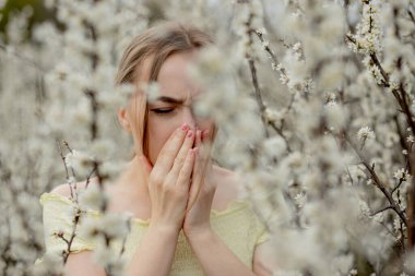 Genç kız sümkürme ve çiçek açan ağacın önünde mendile hapşırma. İnsanları etkileyen mevsimsel alerjik maddeler. Güzel bayanın rhinitis 'i var..