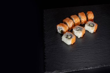 Siyah arka planda somon, peynir ve salatalıklı Philadelphia dürümü. Suşi Philadelphia.