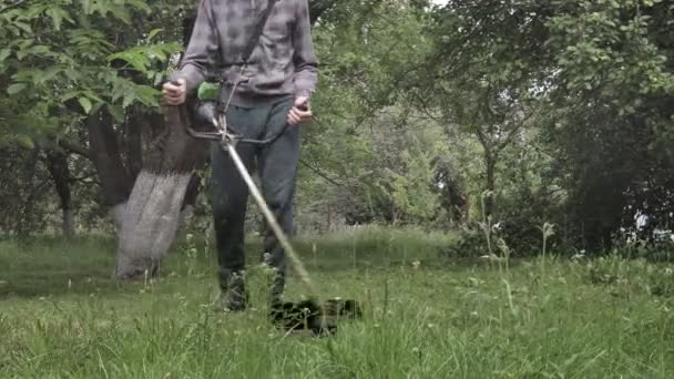 Lavoratore con una falciatrice in mano, falciava erba davanti alla casa. Trimmer nelle mani di un uomo. Giardiniere che taglia l'erba. Stile di vita — Video Stock