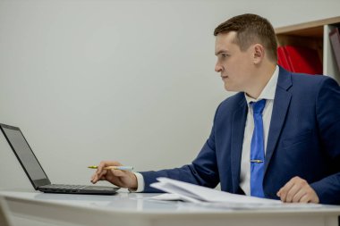 Evde dizüstü bilgisayar ve kağıtlarla çalışan genç bir iş adamı..