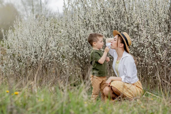 Mutlu anne ve oğul birlikte eğleniyor. Anne oğluna nazikçe sarılıyor. Arka planda beyaz çiçekler açar. Anneler Günü..