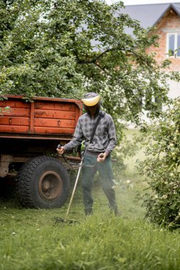 Elinde çim biçme makinesiyle evin önünde çim biçen bir işçi. Bir adamın ellerinde budayıcı. Bahçıvan çimleri biçiyor. Yaşam biçimi