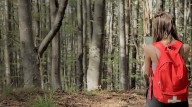 Ormanın ortasında duran bir kadın, akıllı telefonda navigasyon uygulaması kullanıyor, haritanın yardımıyla rotayı takip ediyor, cihaz ekranına bakıyor, ormanda kendini kaybederken akıllı telefon navigasyonunu kullanıyor..