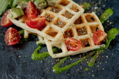 Taze pişmiş Belçika waffle 'ı roka, domates ve siyah bir tabakta avokado. Lezzetli waffle. Kahvaltı konsepti. Sağlıklı kahvaltı..