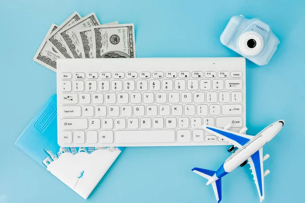 Booking and search flight ticket air international travel concept, keyboard, passport, dollars and airplane on blue background. Summer or vacation concept. Copy space