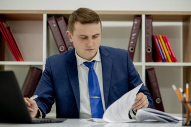 Belgelerle çalışan genç işadamı dosyalara bakıyor, büro masasında oturuyor..