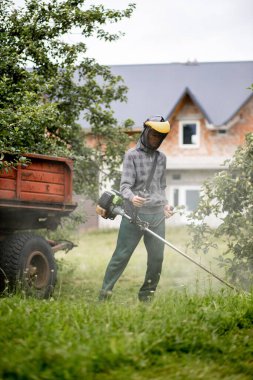 Elinde çim biçme makinesiyle evin önünde çim biçen bir işçi. Bir adamın ellerinde budayıcı. Bahçıvan çimleri biçiyor. Yaşam biçimi