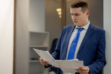 Belgelerle çalışan genç işadamı dosyalara bakıyor, büro masasında oturuyor..