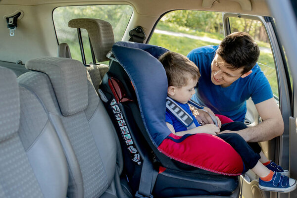 Close-up shot of concentrated father helping his son to fasten belt on car seat. Child transportation safety.