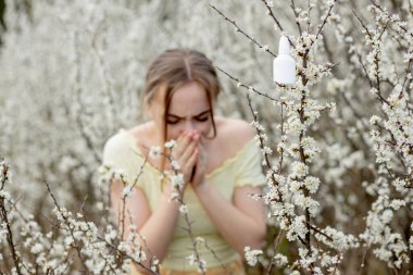 Genç kız sümkürme ve çiçek açan ağacın önünde mendile hapşırma. İnsanları etkileyen mevsimsel alerjik maddeler. Güzel bayanın rhinitis 'i var..