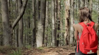 Ormanın ortasında duran bir kadın, akıllı telefonda navigasyon uygulaması kullanıyor, haritanın yardımıyla rotayı takip ediyor, cihaz ekranına bakıyor, ormanda kendini kaybederken akıllı telefon navigasyonunu kullanıyor.