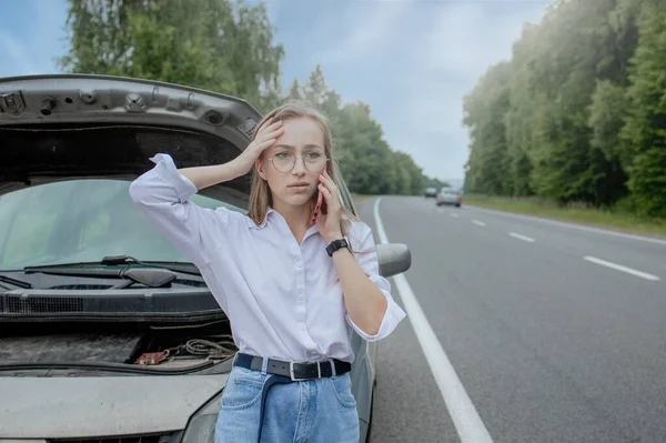 Kaputu patlamış, bozuk bir arabanın yanında duran genç bir kadın aracıyla sorun yaşıyor. Çekici ya da teknik destek bekliyoruz. Bir kadın servis merkezini arıyor..
