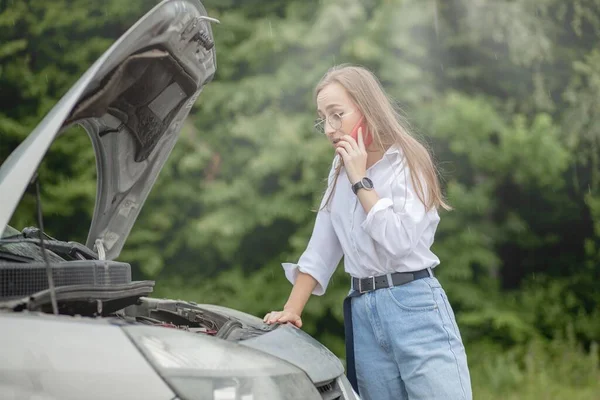 若い女性が壊れた車のボンネットを開けると 彼女の車に問題があった 心配している女性壊れた車の近くの電話で話している 自動車サービスのための壊れた車の呼び出しの近くに立つ女の子モデル — ストック写真