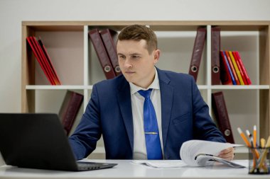 Belgelerle çalışan genç işadamı dosyalara bakıyor, büro masasında oturuyor..