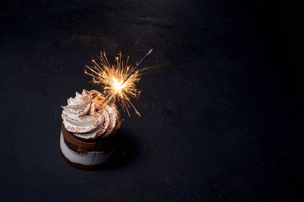 Delicious birthday cupcake with firework candle on table against dark background