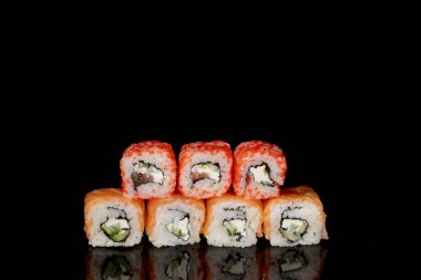 Philadelphia rulosu somon, peynir ve salatalık ile siyah arka planda yansımalı. Suşi Philadelphia.