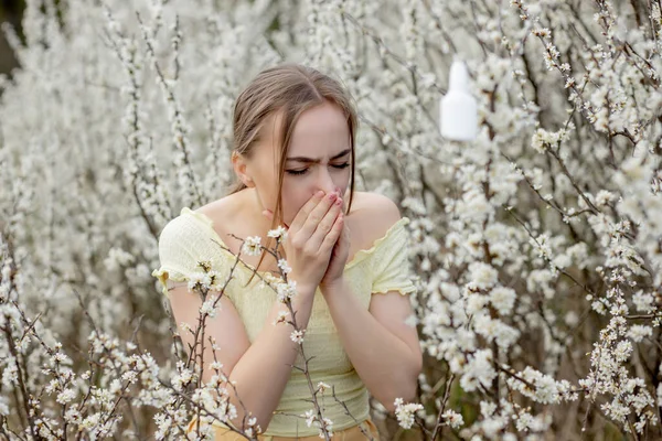 花の木の前で鼻を吹いてティッシュでくしゃみをする若い女の子 季節性アレルゲンが人々に影響を与えます 美しい女性は鼻炎を持っている — ストック写真