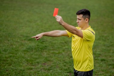 Kızgın futbol hakemi kırmızı kart gösteriyor ve penaltıyı eliyle işaret ediyor..