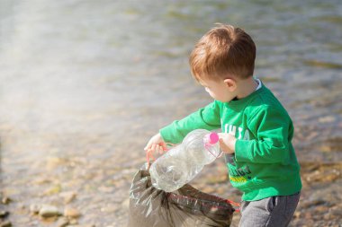 Çevre kavramını kaydedin, küçük bir çocuk çöpleri ve plastik şişeleri toplayıp çöpe atıyor.