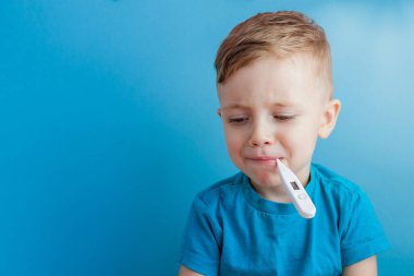 Termometresi olan hasta bir çocuk ateşinin yüksekliğini ölçüyor ve kameraya bakıyor..