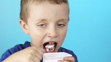 Mavi arka planda yoğurt yiyen küçük çocuk..