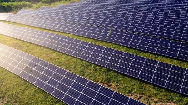 Solar Power Station in Green Field on Sunny day. Aerial view. Solar Panels Stands in a Row in Field for Power Production. Drone fly over Solar Farm. Renewable green energy. Alternative energy sources