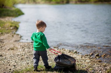 Çevre kavramını kaydedin, küçük bir çocuk çöpleri ve plastik şişeleri toplayıp çöpe atıyor.