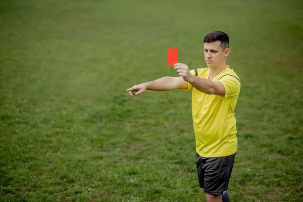 Angry football referee showing a red card and pointing with his hand on penalty.