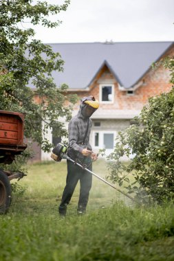 Elinde çim biçme makinesiyle evin önünde çim biçen bir işçi. Bir adamın ellerinde budayıcı. Bahçıvan çimleri biçiyor. Yaşam biçimi