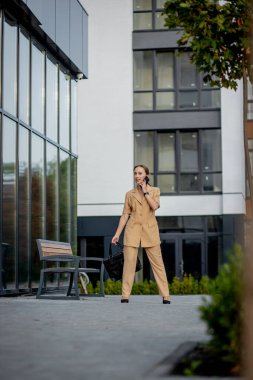 Ofis binasının önünde dikilen ve cep telefonuyla konuşan bir iş kadınının portresi..