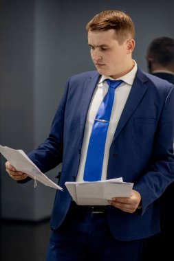 Belgelerle çalışan genç işadamı dosyalara bakıyor, büro masasında oturuyor..