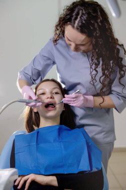 Sağlık kontrolü. Stomatoloji merkezindeki dişçi kadın dişlerini diş aletleri kullanarak inceliyor..