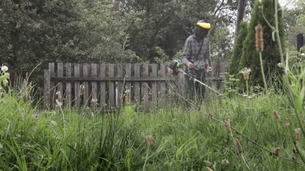 Pracownik kosi wysoką trawę elektryczną lub benzynową przycinarką do trawników. Narzędzia i sprzęt do pielęgnacji ogrodu. Proces przycinania trawników kosiarką ręczną — Wideo stockowe