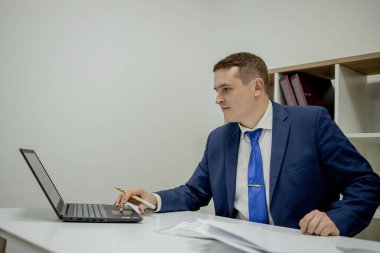 Evde dizüstü bilgisayar ve kağıtlarla çalışan genç bir iş adamı..