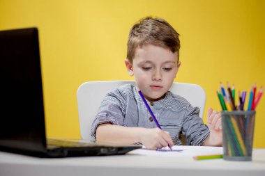 Mutlu Çocuk sarı arka planda ödev yaparken dijital dizüstü bilgisayar kullanıyor. Sosyal Mesafe, E-öğrenim çevrimiçi eğitim.