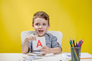 Mutlu gülümseyen küçük anaokulu çocuğu, okul başlamadan önce ev ödevlerini yapan mektupları evde gösteriyor. Çocuklar için İngilizce öğrenme.