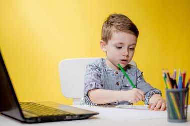Mutlu Çocuk sarı arka planda ödev yaparken dijital dizüstü bilgisayar kullanıyor. Sosyal Mesafe, E-öğrenim çevrimiçi eğitim.