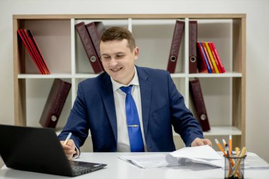 Evde dizüstü bilgisayar ve kağıtlarla çalışan genç bir iş adamı..