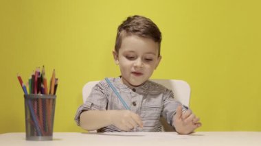 Masada gülümseyen küçük çocuk sarı arka planda annesi için pastel boyalarla resim çiziyor. Yaratıcılık konsepti. Okula geri dön.