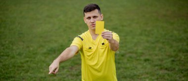 Kızgın futbol hakemi sarı kart gösteriyor ve penaltıyı eliyle işaret ediyor..