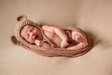 Yeni doğan, örgü şapkalı uyuyan bebek kahverengi kumaşın üzerinde yatıyor..