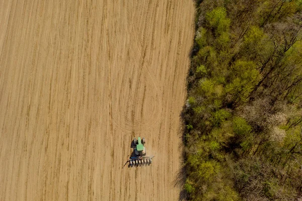 Aerial view large tractor cultivating a dry field. Top down aerial view tractor cultivating ground and seeding a dry field. Aerial tractor cuts furrows in farm field for sowing.