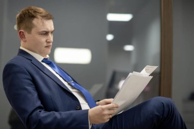 Belgelerle çalışan genç işadamı dosyalara bakıyor, büro masasında oturuyor..