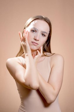 Yüzünde kahverengi bir arka planda kozmetik maske olan genç bir kadın. Deri durumunu iyileştirmek için yüz maskesi. Yüz bakımı. Kozmetik gevşeme.