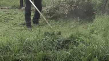 Elektrikli çim biçme makinesiyle çim biçen bir işçi. Bahçıvanlık malzemeleri ve ekipmanlar. Çim biçme makinesiyle çim biçme işlemi.