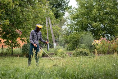 Elinde çim biçme makinesiyle evin önünde çim biçen bir işçi. Bir adamın ellerinde budayıcı. Bahçıvan çimleri biçiyor. Yaşam biçimi